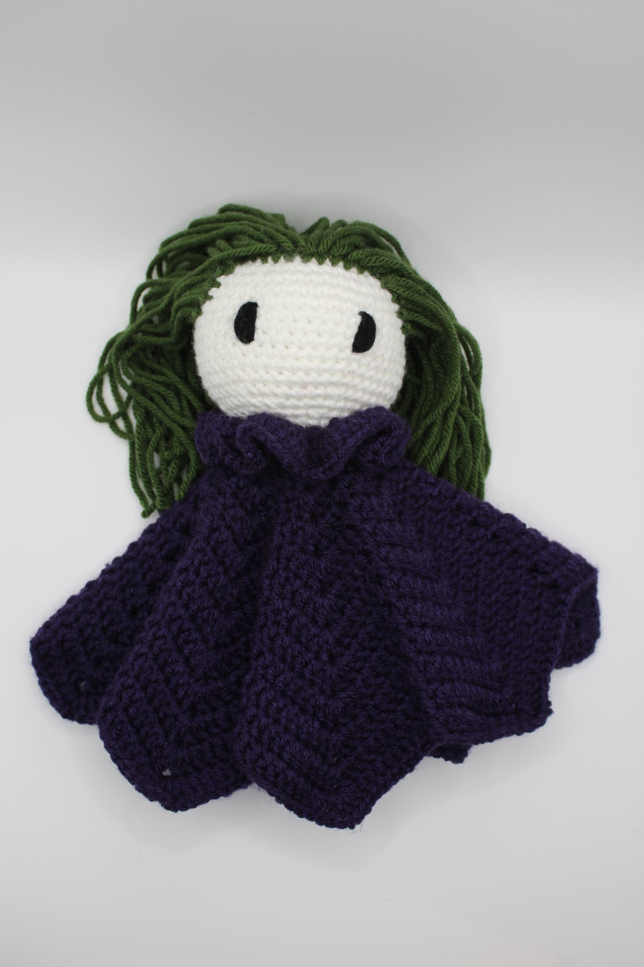 Crochet doll with green hair and purple outfit on a white background