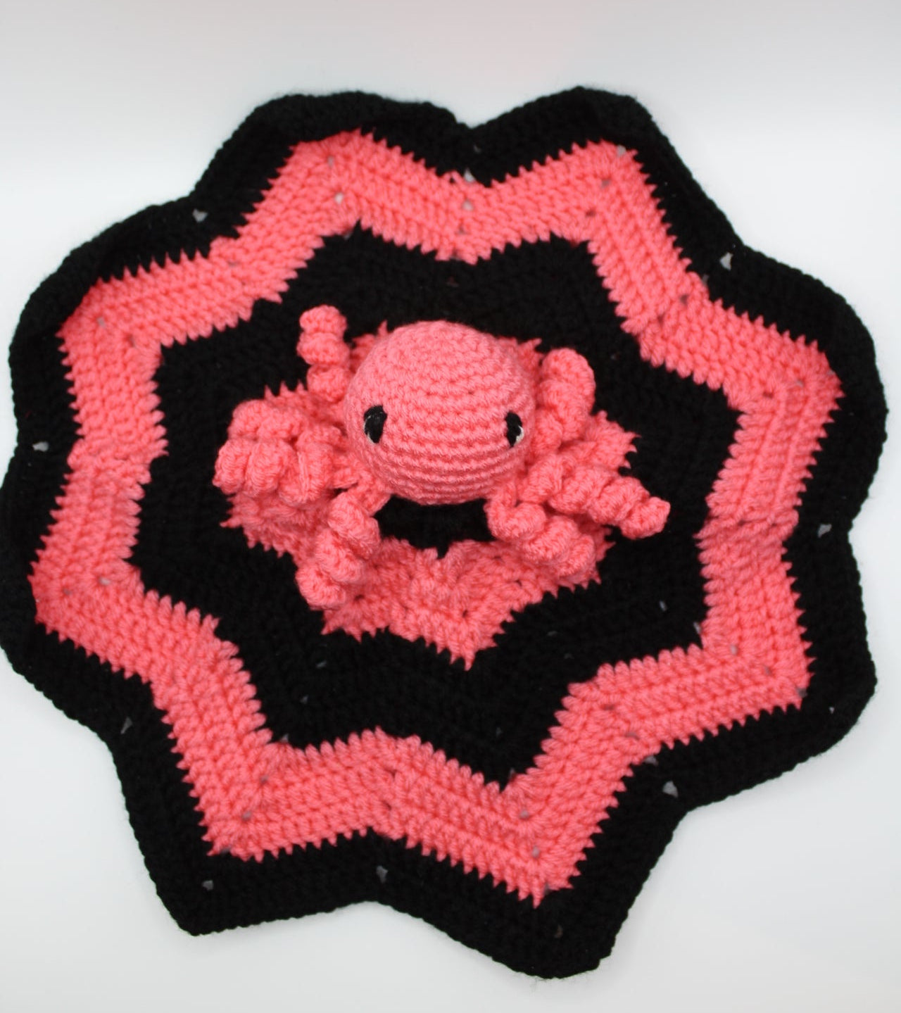 Crocheted pink and black patterned item on a white background