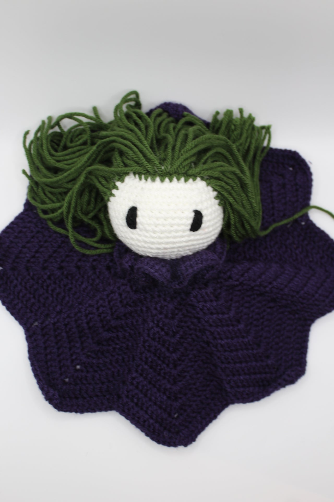 Crocheted clown lovey with green hair and white face.
